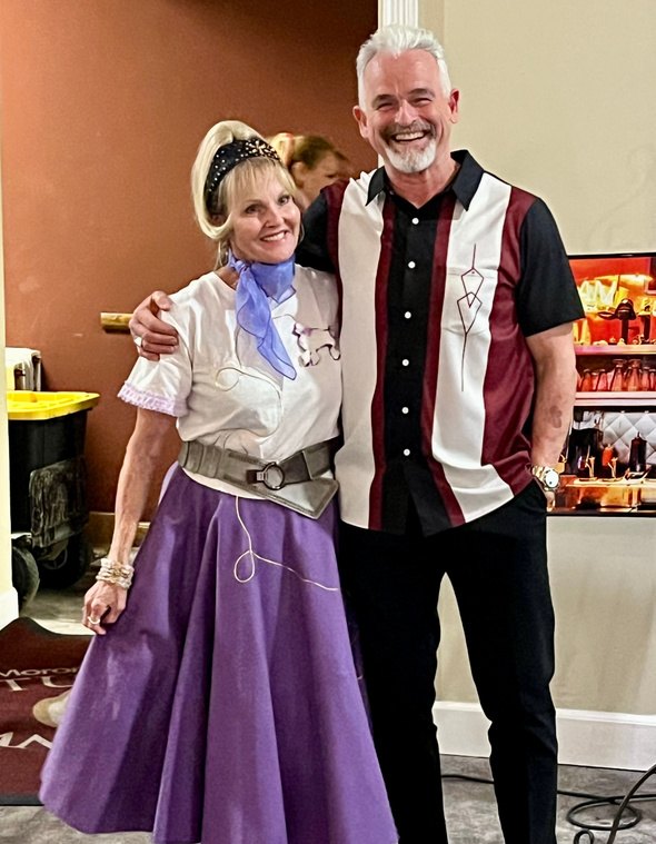 A couple in matching purple-skirt-and-bowling-shirt fifties attire