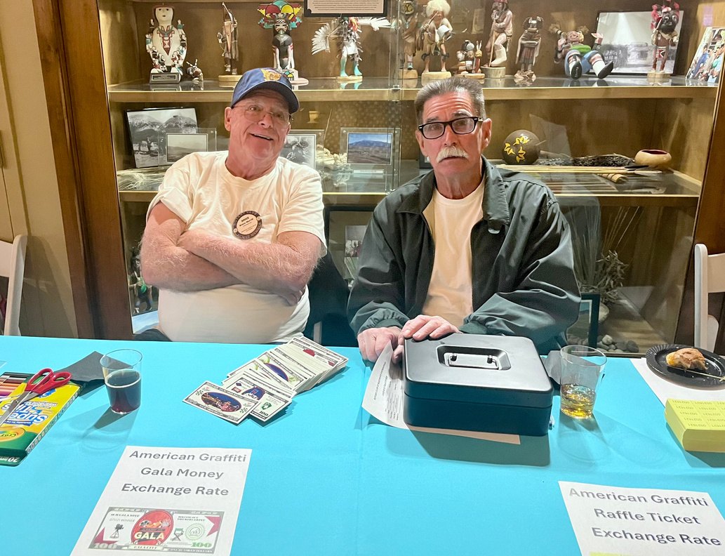 Two members staffing the cash table beside silent auction signage