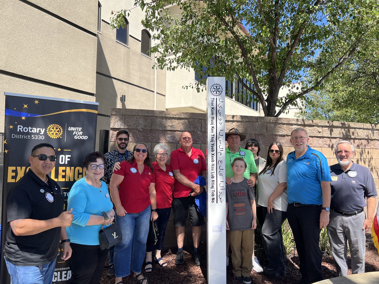Club members and their families gather around the new Peace Pole, inscribed &ldquo;May Peace Prevail on Earth&rdquo; in several languages, beside the Rotary District 5330 banner